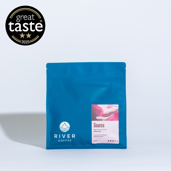 Blue coffee bag with 'River Coffee' branding and 'Great Taste' award on a light gray background