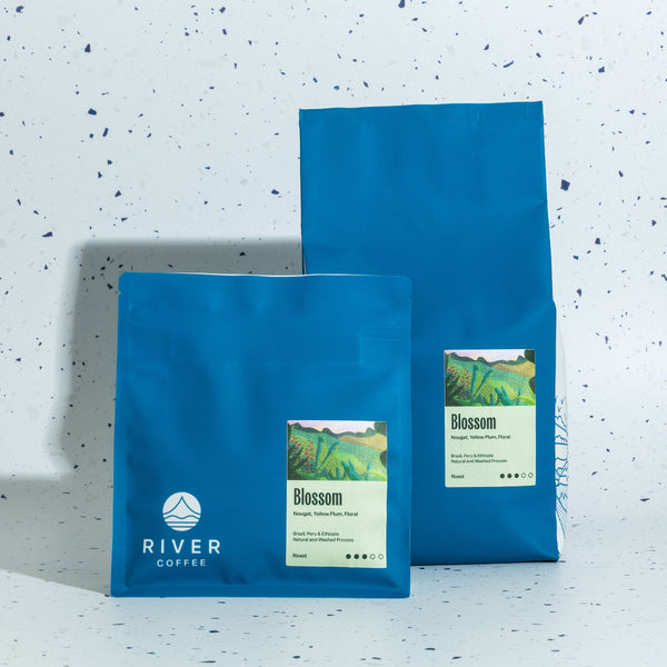 Two blue coffee bags with 'River Coffee' branding on a speckled white background
