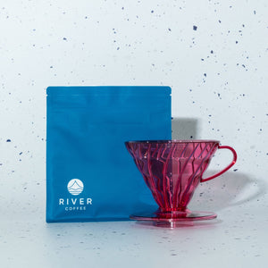 Red coffee dripper and blue River Coffee package on a speckled white background