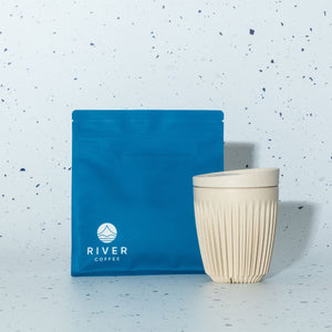 Blue coffee bag and beige ceramic cup on a light blue speckled background